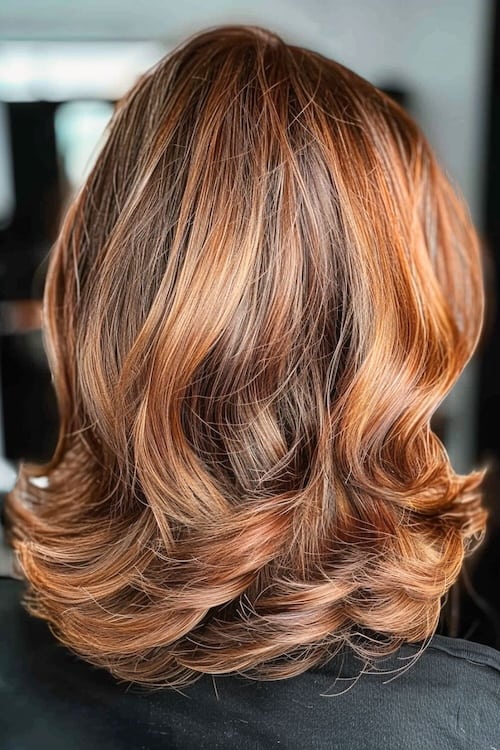 Subtle layered waves with copper balayage highlights medium-length haircut.