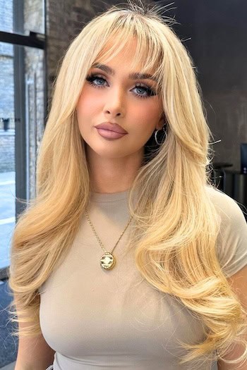 Golden Blonde Waves With Feathered Bangs Hairstyle on a woman with long blonde hair.