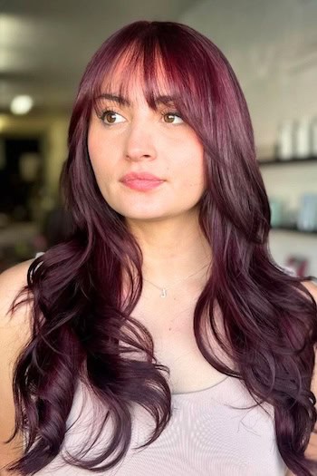 Plum Waves With See-Through Bangs Hairstyle on a smiling woman with long plum hair.