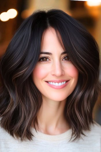 Shoulder-Length Layers With Subtle Highlights Haircut on a smiling woman with dark brown hair and subtle highlights.