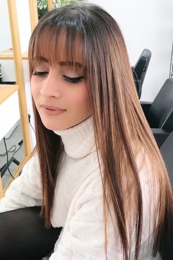 Smooth Long Hair With See-Through Bangs Hairstyle on a smiling woman with long brown hair looking down.