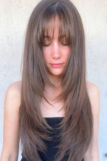 Straight Layered Hair With Piecey Bangs Hairstyle on a smiling woman with long brown hair looking down.