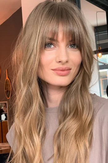 Textured Long Waves With Straight Bangs Hairstyle on a smiling woman with long light brown hair.