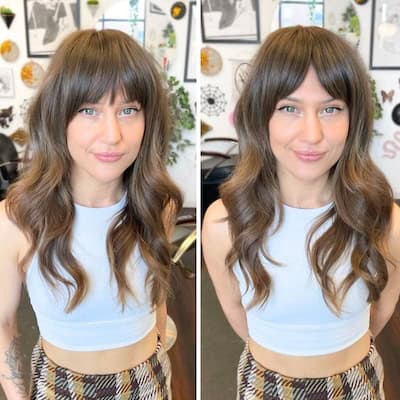 Two side-by-side images of Long Wavy Layers With Full Bangs And Curtain Bangs Hairstyle on a smiling woman with long brown hair.