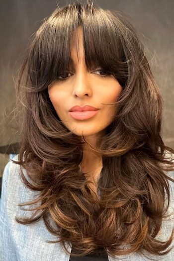 Voluminous Curled Layers With Curtain Bangs Hairstyle on a woman with long brown hair.