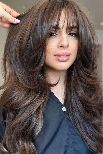 Voluminous Layers With Wispy Bangs Hairstyle on a woman with long brown hair.