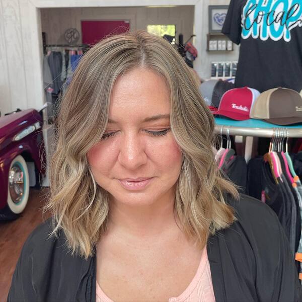 a woman inside a salon wearing a black cape having her hair styled into sandy blonde with lowlights