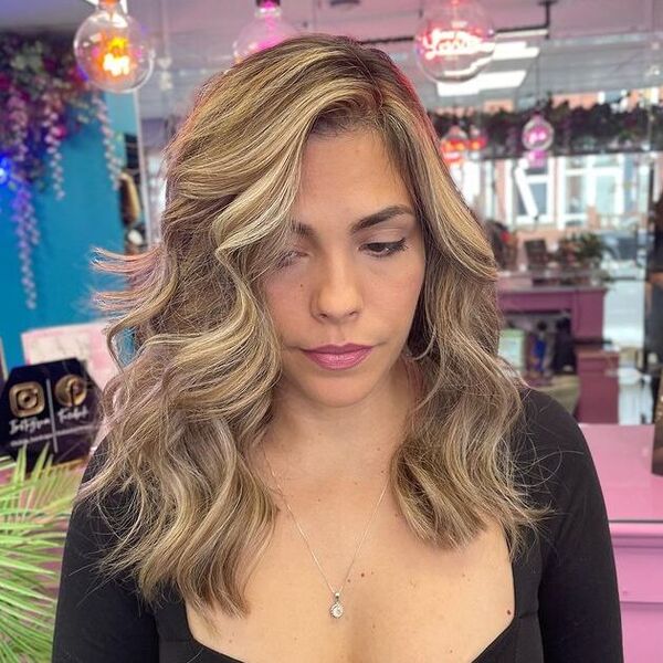 a woman inside a salon wearing a black longsleeve top having her sunny blonde highlights for brown hair