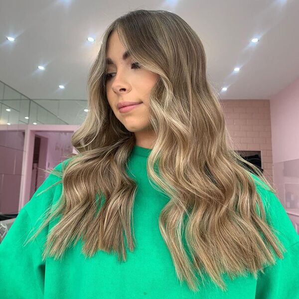 a woman inside a salon wearing a green longsleeve having her sandy ash brown hair