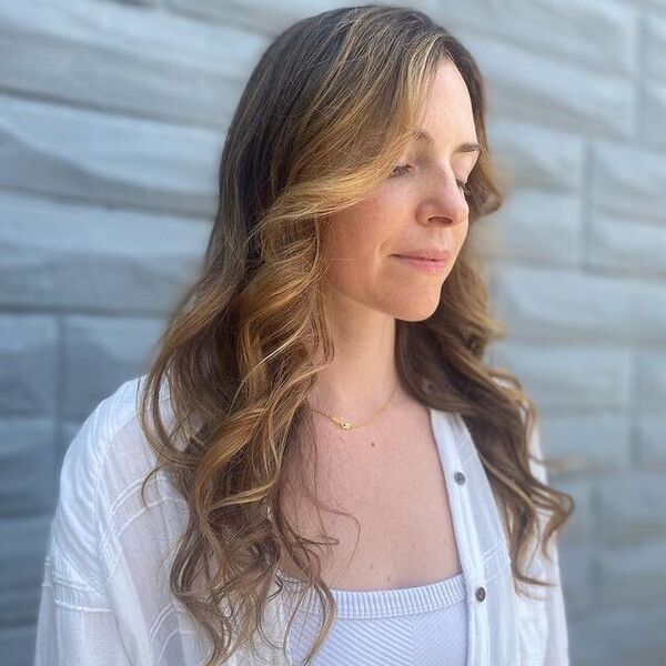 a woman wearing a white top with white longsleeve blazer having her caramel brown money piece hair