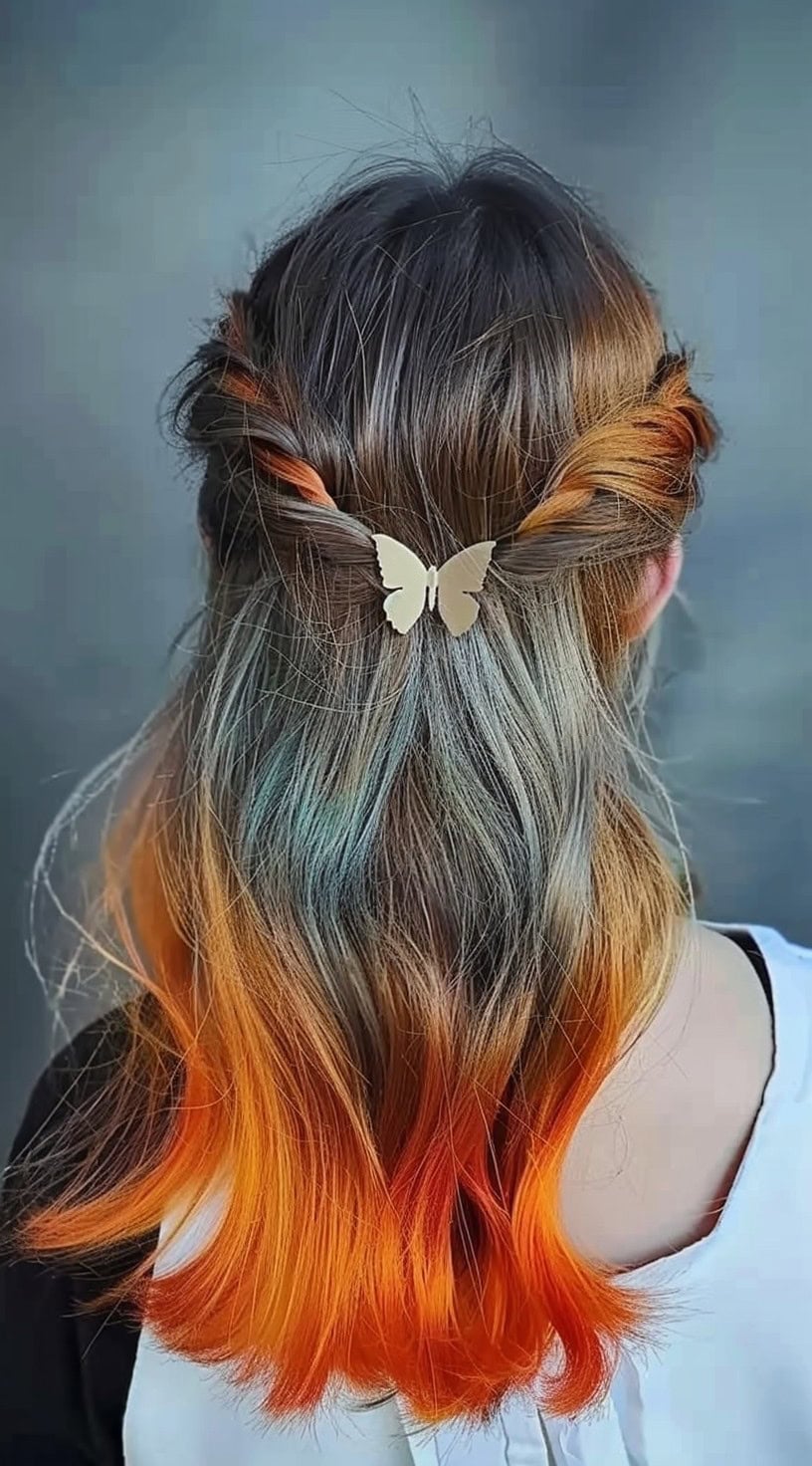 A woman with long hair styled half-up has orange ombre highlights that transition from dark roots to bright ends.