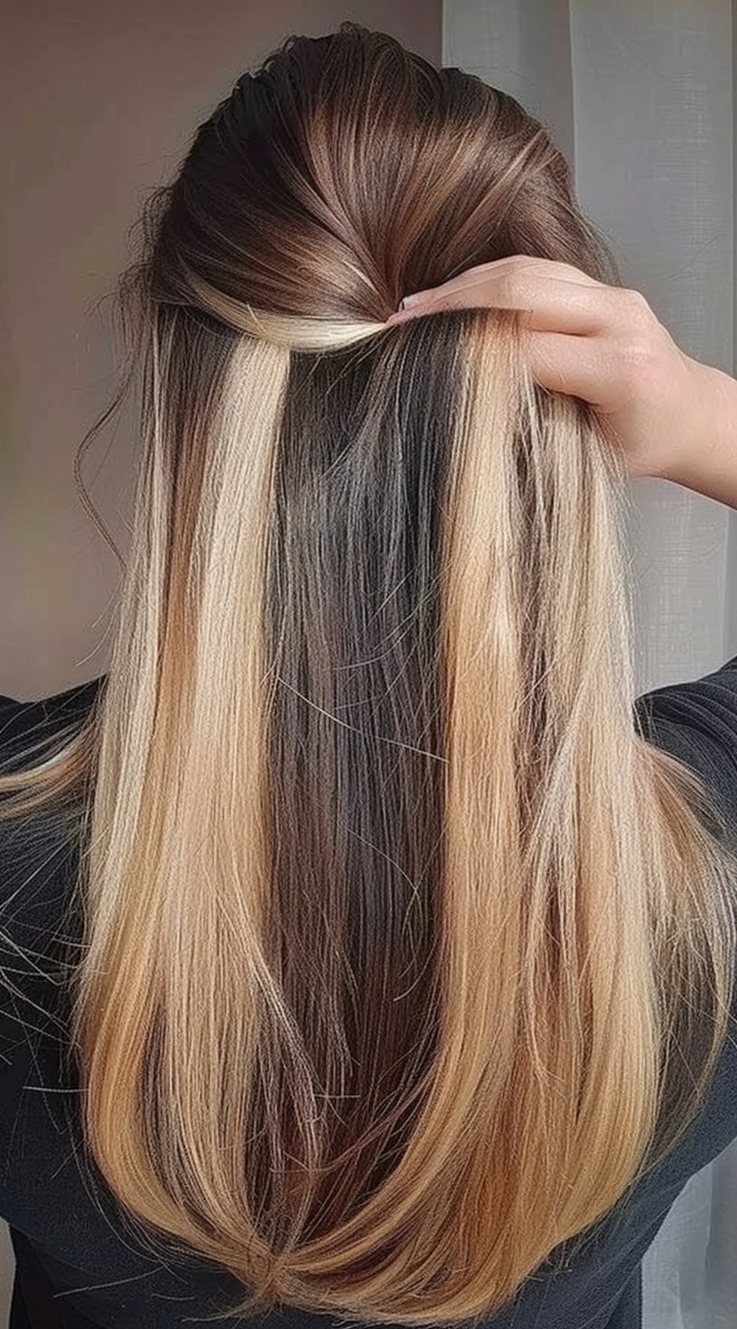 In this photo, a person is holding up their long, dark hair to reveal blonde peekaboo highlights underneath.