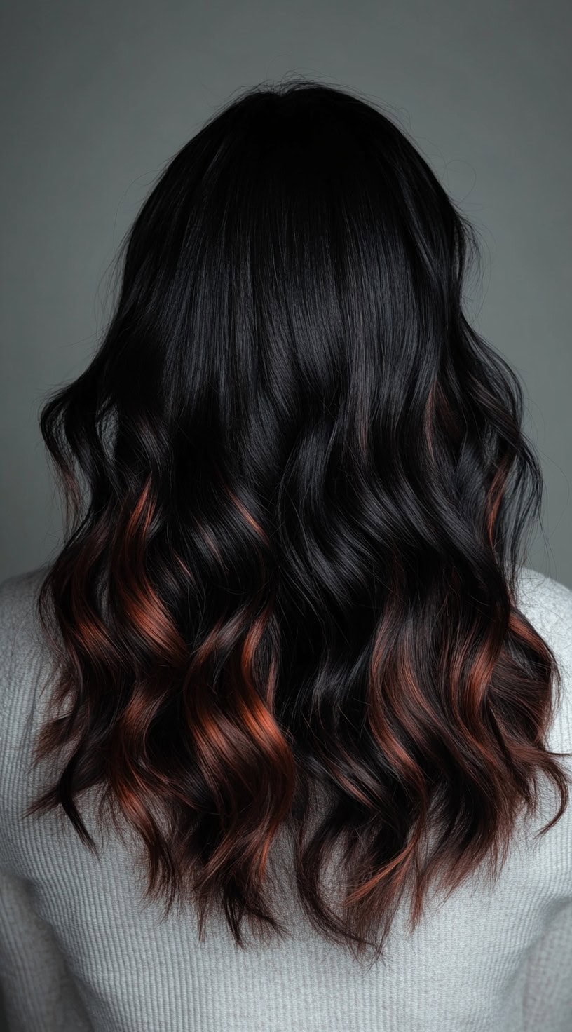 In this photo, dark brown wavy hair is subtly enhanced with copper balayage starting at the mid-length, giving a delicate touch of color.