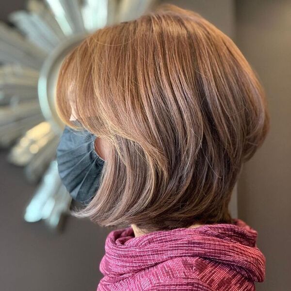 Medium Layered Hair with Light Brown - a woman wearing a black facemask and a pink sweater