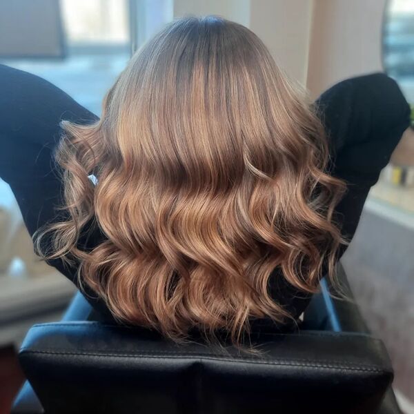 Wavy Light Caramel Brown Hair - a woman sitting on a salon chair